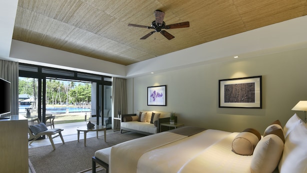 Una habitación de hotel con una cama grande, un escritorio, una silla, un sofá y un ventilador de techo.