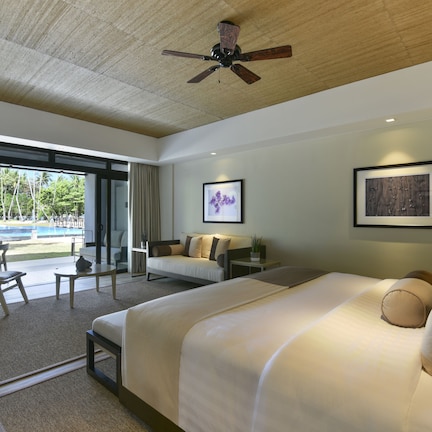 A hotel room with a large bed, a desk, a chair, a sofa, and a ceiling fan.