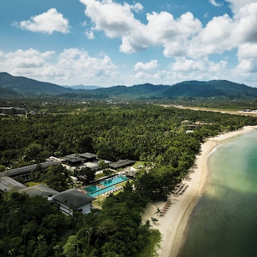 A coastal resort with a swimming pool, beachfront, and lush greenery.