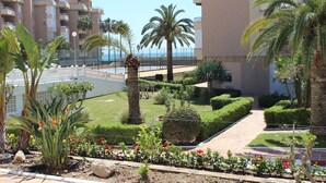 A landscaped garden with palm trees, a pathway, and a view of a building with balconies. - Fantastic oceanfront apartment (Torrox Costa)