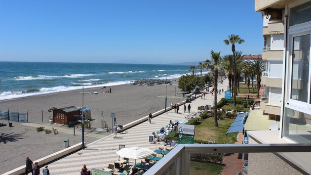 A beachside view with a building, palm trees, and a clear sky. - Fantastic oceanfront apartment (Torrox Costa)