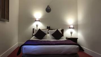 A neatly made bed with a purple blanket, two bedside lamps, and a wall-mounted clock.