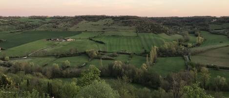 A rural landscape with rolling green fields, a few scattered buildings, and a clear sky.