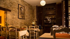 Un comedor con pared de piedra, sillas de madera, una mesa con mantel blanco y una araña.