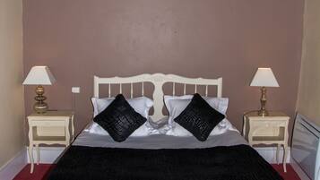 A neatly made bed with a black bedspread and two black pillows, flanked by two bedside tables with lamps, in a room with a red carpet and wooden ceiling beams.