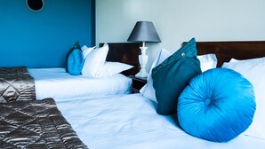 Habitación de hotel con dos camas, una mesita de noche, una lámpara y un espejo redondo en la pared.