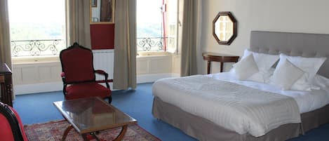 Un dormitorio con una cama grande, una silla roja, una mesa de vidrio y vistas al exterior.