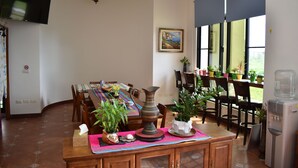 A dining area with a table set for four, surrounded by chairs, a water dispenser, and potted plants. - Longman Villa (Huxi)