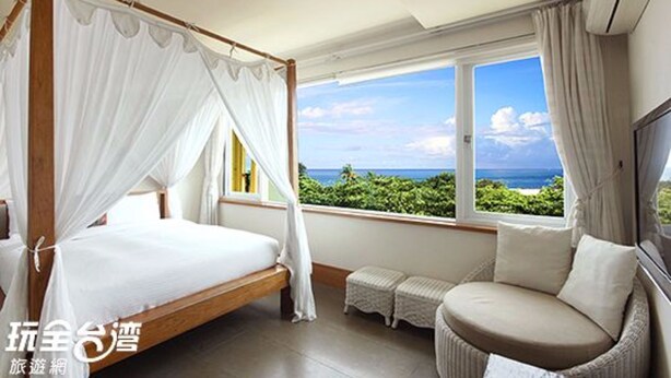A bedroom with a four-poster bed, a small seating area, and a large window with a view of the ocean. - Daban Six Guest House (Hengchun)