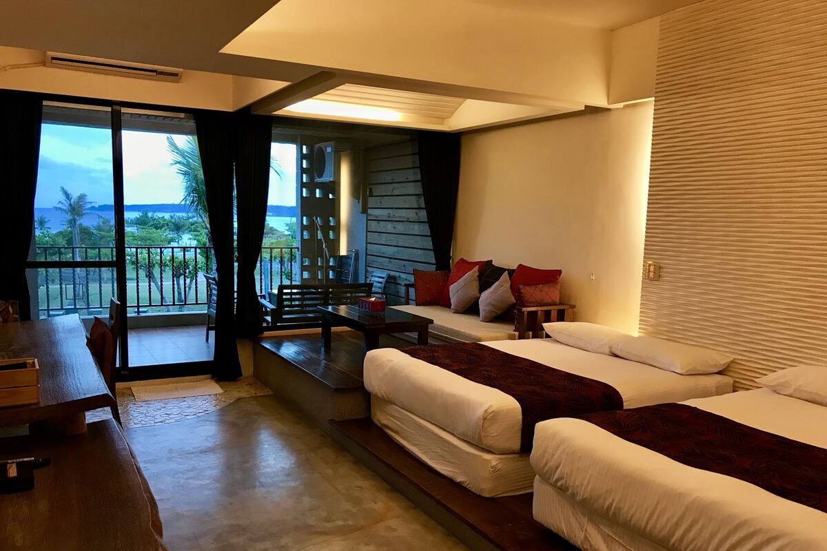 A hotel room with a balcony, a dining table, and two beds.