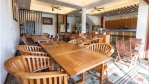 A spacious dining area with wooden tables and chairs, a ceiling fan, and a view of the kitchen in the background. - Daban Six Guest House (Hengchun)