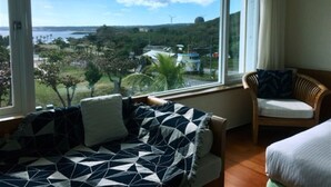 A room with a large window offering a view of the sea and greenery, a sofa with patterned cushions, and a wooden chair. - Daban Six Guest House (Hengchun)