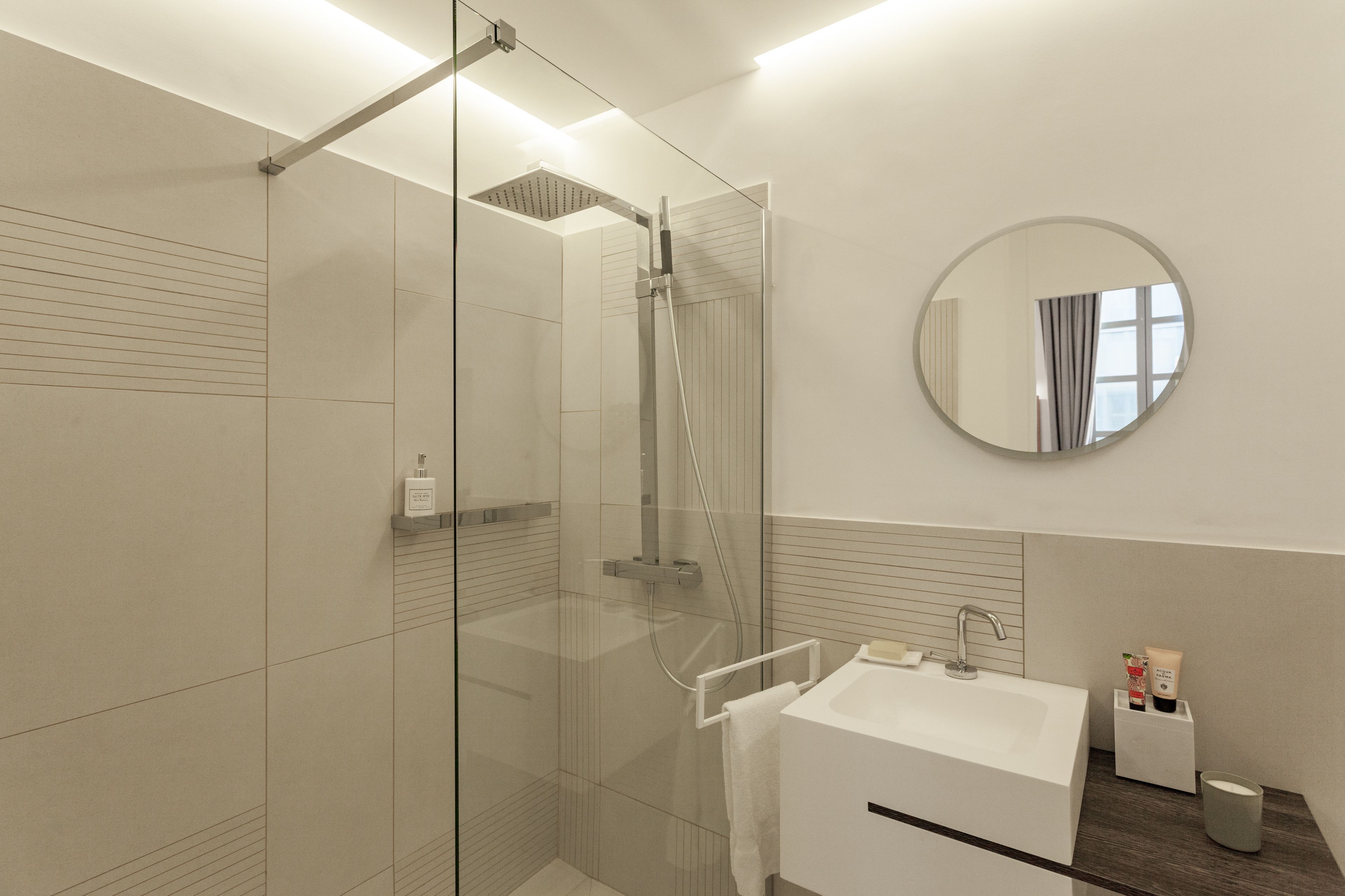 Een moderne badkamer met een douchecabine van glas, een witte wastafel en een ronde spiegel.