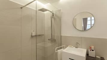 Een moderne badkamer met een douchecabine van glas, een witte wastafel en een ronde spiegel.