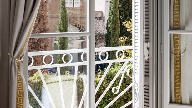 A balcony with white balustrades and a view of a building with shutters and a tree. - Maison du Collectionneur (Aix-en-Provence)
