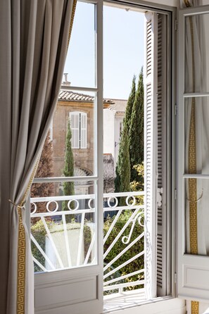 A balcony with white balustrades and a view of a building with shutters and a tree. - Maison du Collectionneur (Aix-en-Provence)