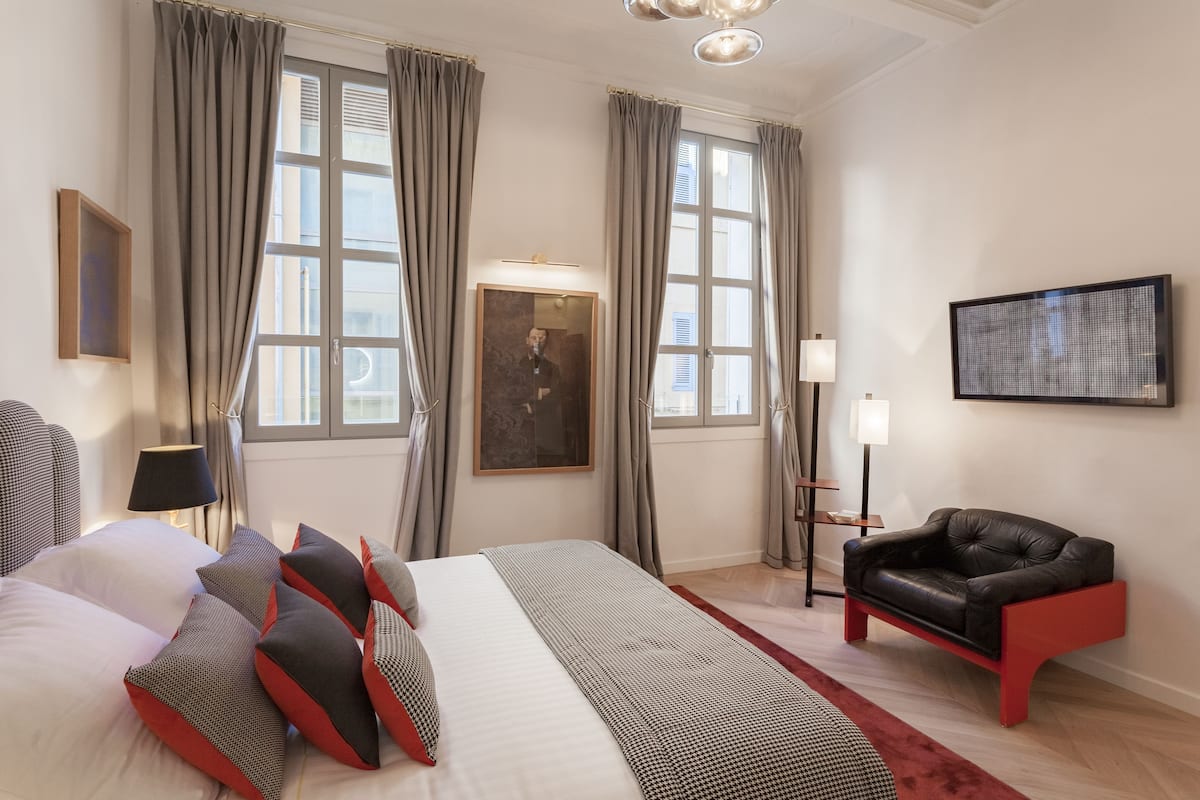 Una habitación de hotel con una cama grande, un sofá de cuero negro y un retrato enmarcado en la pared.