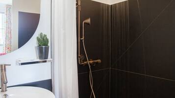 A modern bathroom with a black tiled shower, a white sink, and a mirror.