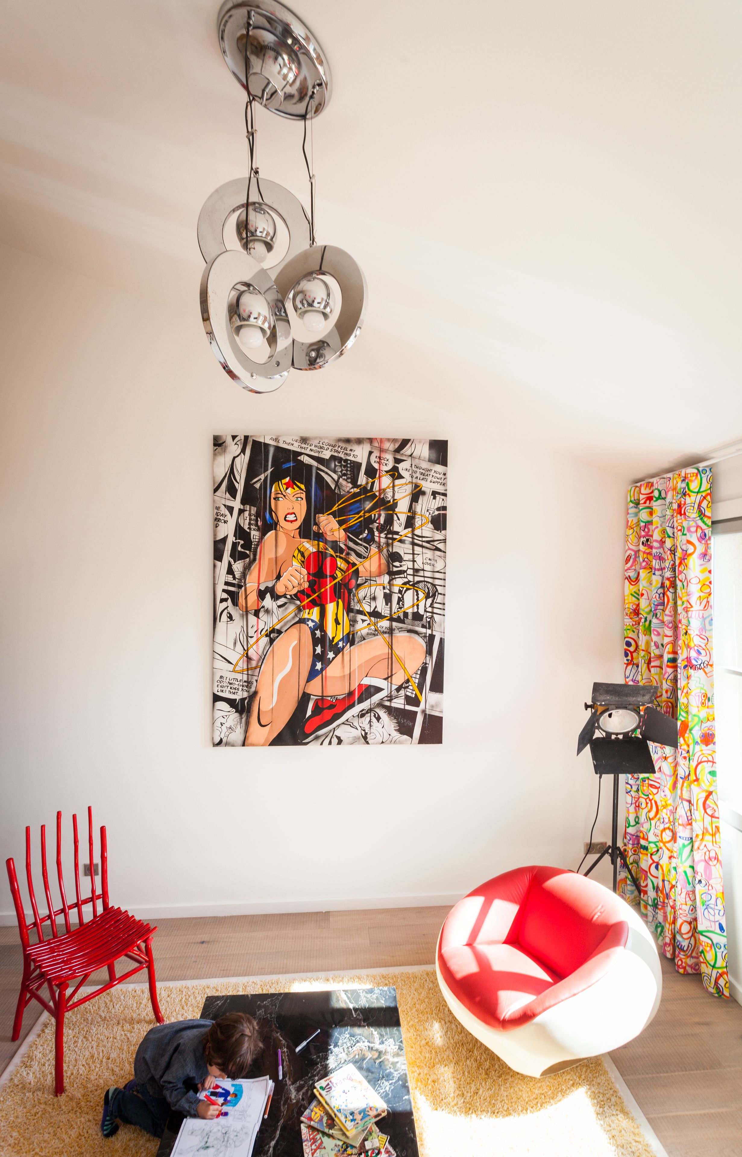 Una sala moderna con un cuadro abstracto grande, una silla roja, una silla roja y blanca peculiar, y un set de batería frente a una cortina colorida.