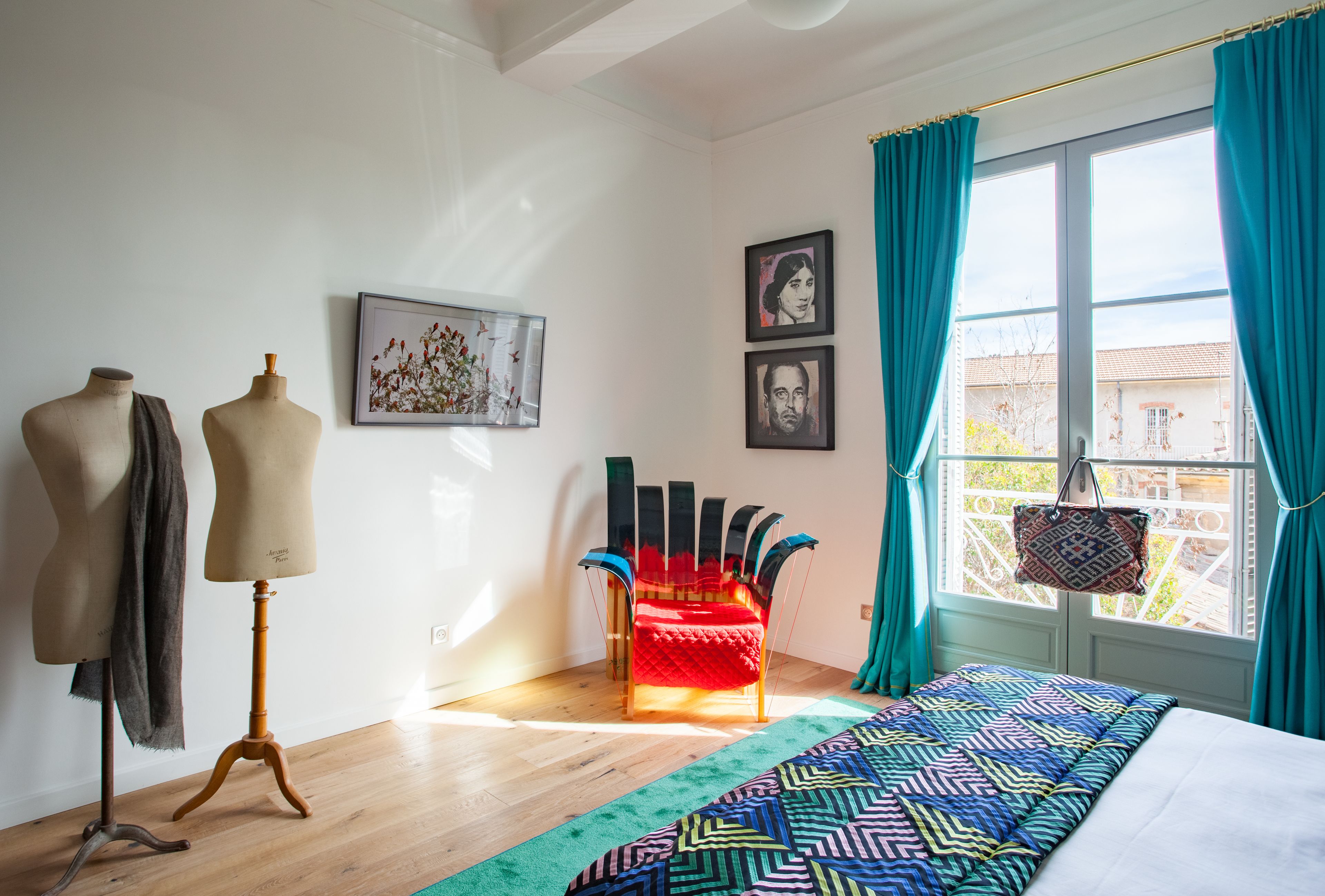 Ein Schlafzimmer mit einem Bett, einem Sessel, einer Mannequin und einem Fenster mit Vorhängen.