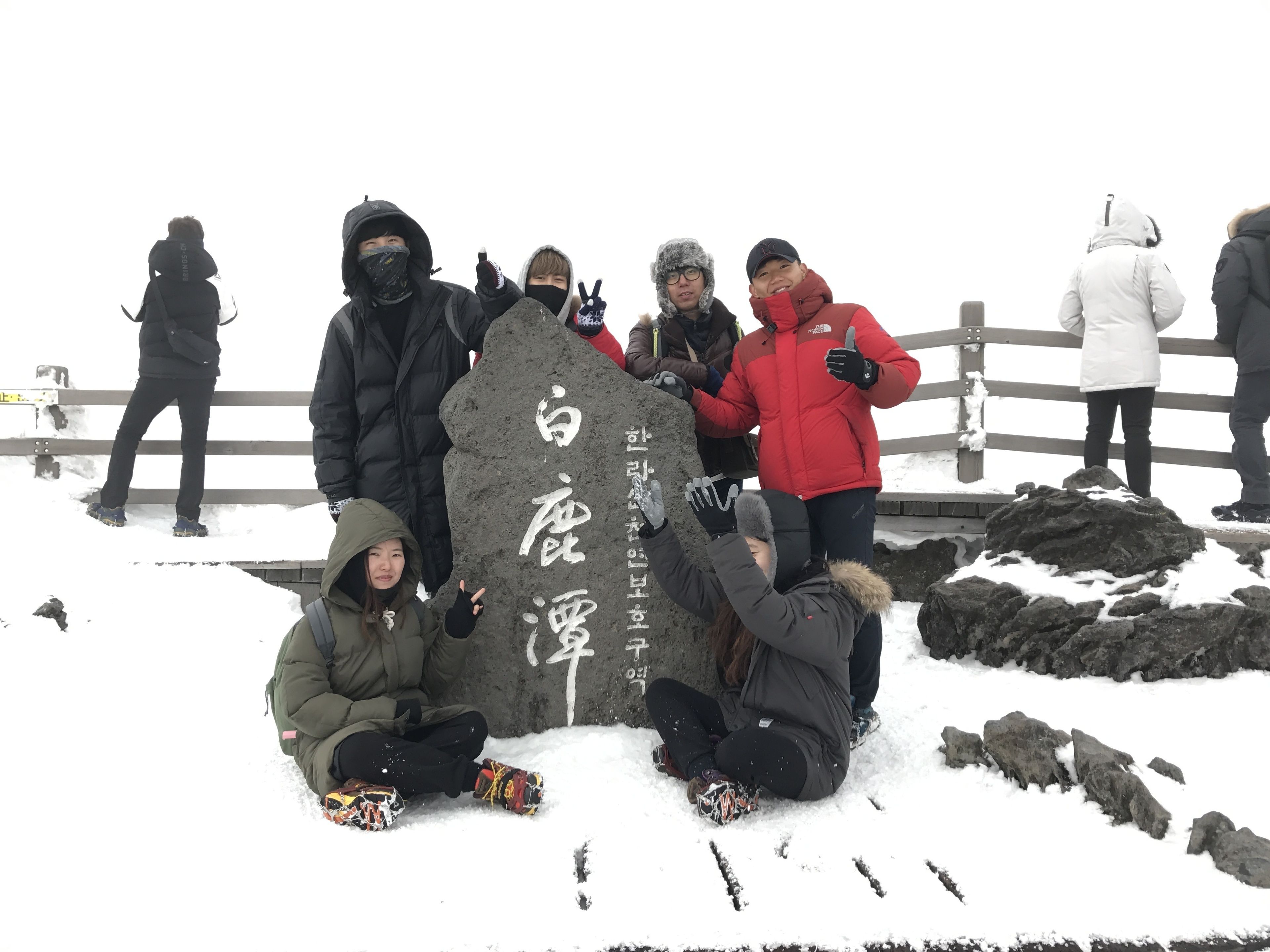 A group of people around a large stone with inscriptions, sitting on the snow.
