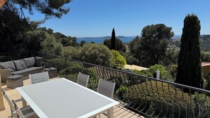 Eine Terrasse mit Tisch und Stühlen mit Blick auf eine schöne Landschaft aus Meer und Hügeln.