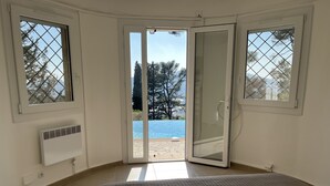 Ein Schlafzimmer mit einem großen Bett, einer Glastür, die zu einem Poolbereich führt, und einem Fenster mit Blick auf Bäume und Berge.