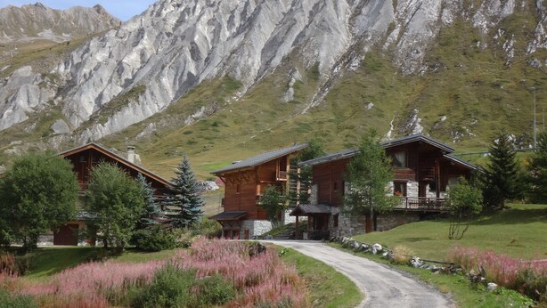 Un rifugio alpino con una strada sterrata che conduce all'ingresso, immerso nel verde e con le montagne rocciose sullo sfondo.