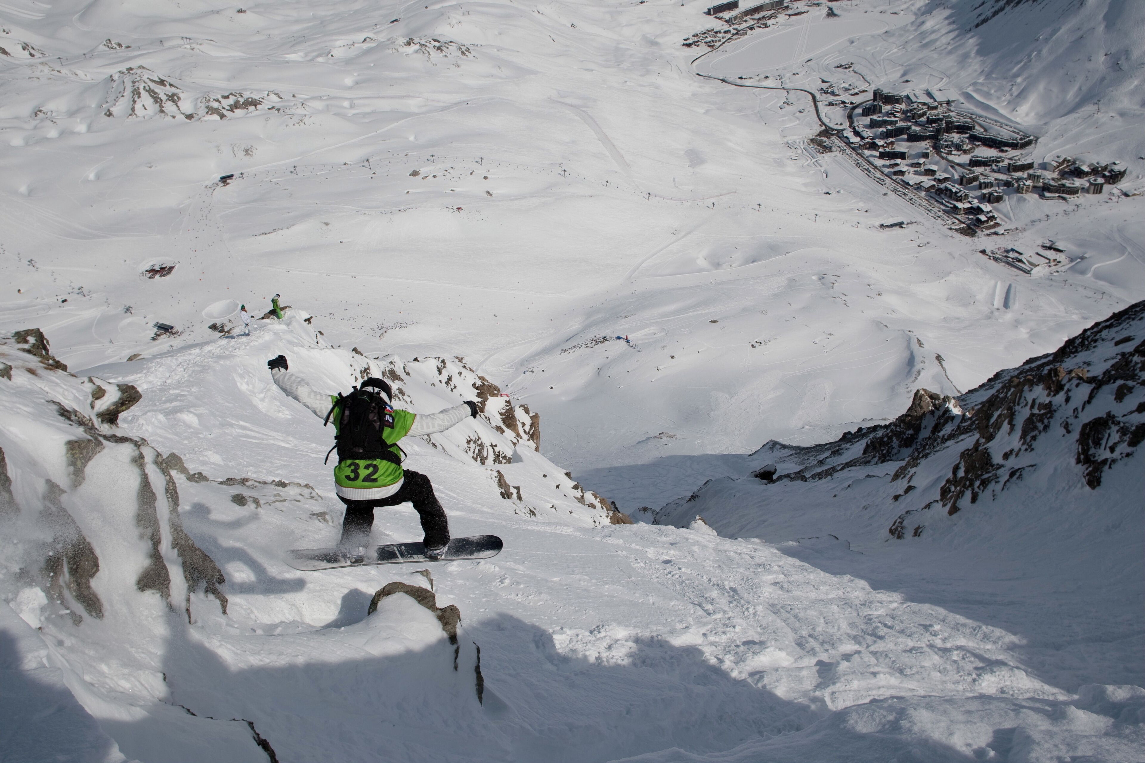 A snowboarder descending a snowy slope with a town in the background.