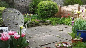 Un patio jardín con suelo de piedra, una silla de metal y diversas plantas en macetas.