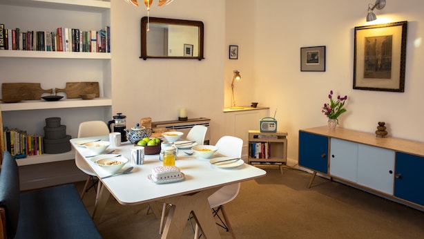 Un comedor con una mesa blanca, sillas y una estantería.