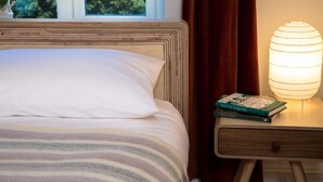 Una cama bien hecha con ropa de cama a rayas, una lámpara de noche y un libro titulado
