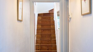 Un pasillo con escalera de madera, paredes blancas y alfombra texturizada.