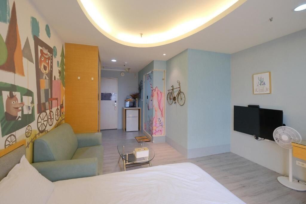 Een hotelkamer met een bed, een kleintje tafel, een bank, een televisie en een ventilator.