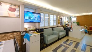 A hotel reception area with a television, seating, a reception desk, and a window with a view of buildings. - 85 Asia Hotel (Kaohsiung)