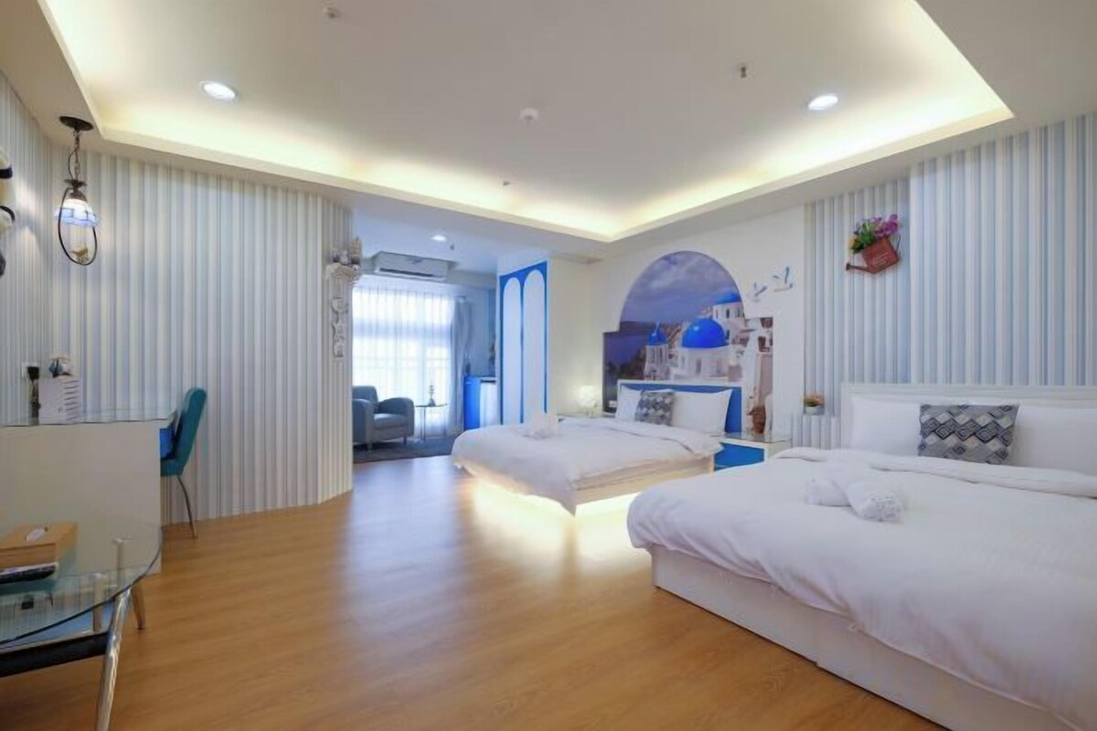 A hotel room with two beds, a desk, and a view of the city.