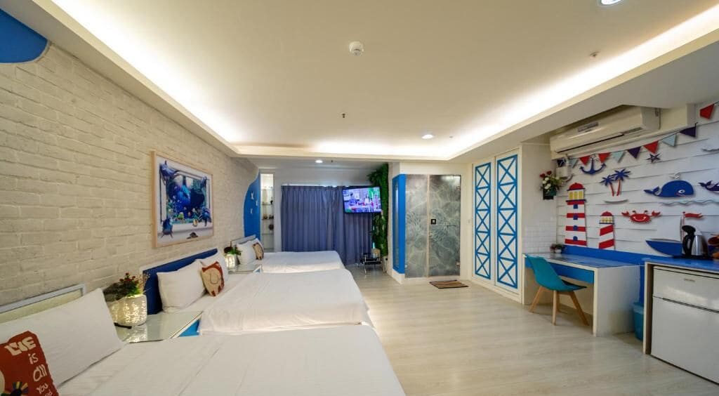 A hotel room with a bed, a desk, a TV, and a kitchen area.