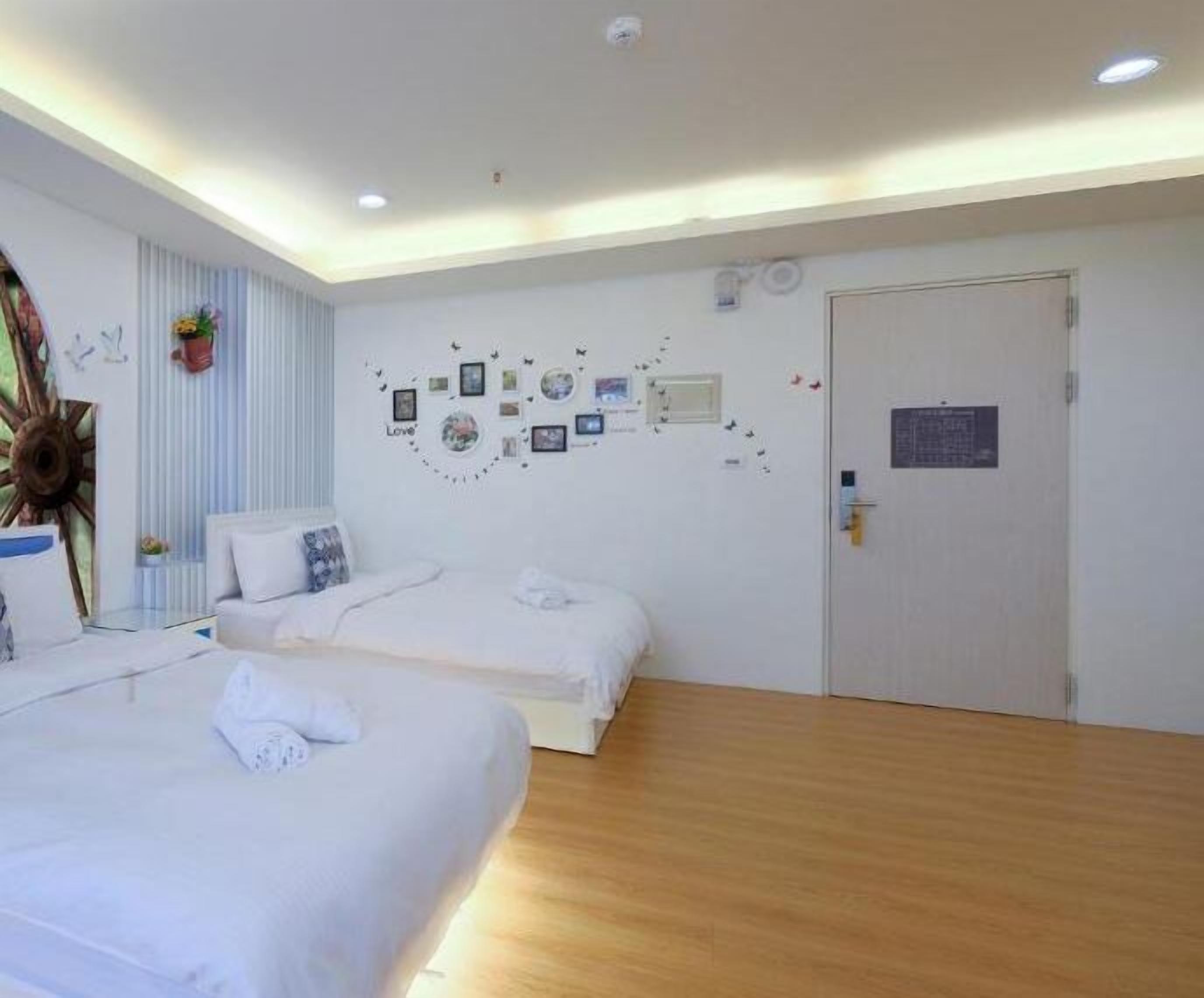 A hotel room with two beds, a wooden floor, a white door, and a wall decorated with pictures and a 'Love' sign.