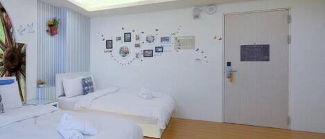 A hotel room with two beds, a wooden floor, a white door, and a wall decorated with pictures and a 'Love' sign.