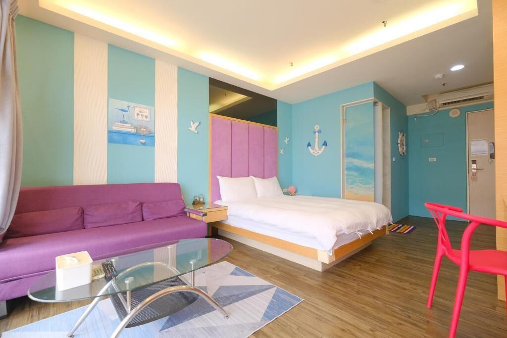 Une chambre à coucher avec un lit, un canapé violet, une table en verre et une chaise rouge.