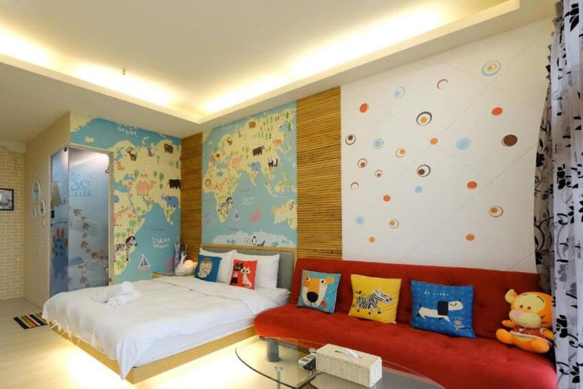 Ein Hotelzimmer mit einem Bett, einem roten Sofa, einer Weltkarte an der Wand und einem kleinen Tisch mit einer Lampe.