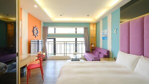 A hotel room with a bed, a desk, a chair, a purple sofa, and a view of the outside. - 85 Asia Hotel (Kaohsiung)