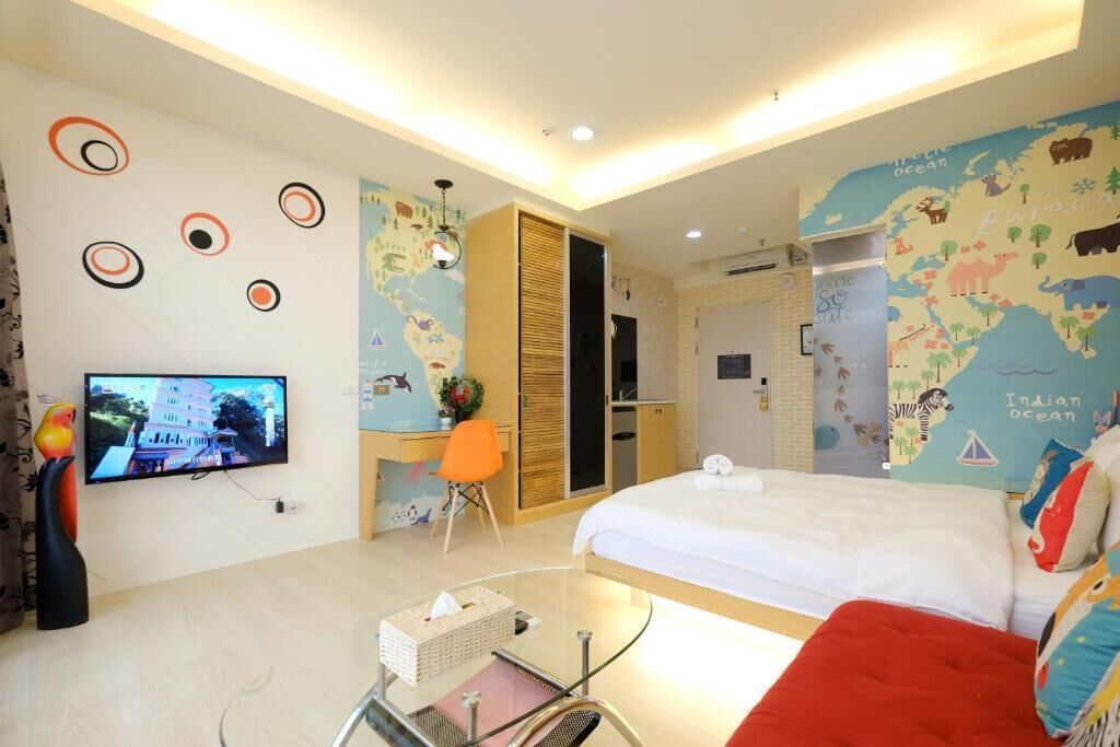 A modern hotel room with a large bed, a TV mounted on the wall, a desk with a chair, and a map mural on the wall.