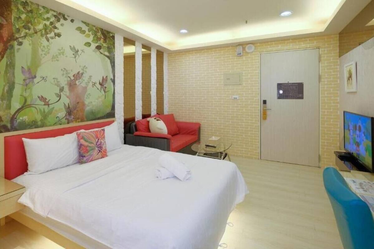Ein Hotelzimmer mit einem großen Bett, einem roten Sofa, einem Fernseher und einem Wandgemälde.