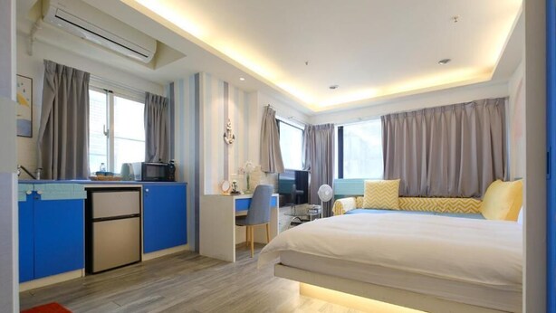 A modern hotel room with a large bed, a desk with a computer, a small kitchenette, and a view of the city. - 85 Asia Hotel (Kaohsiung)