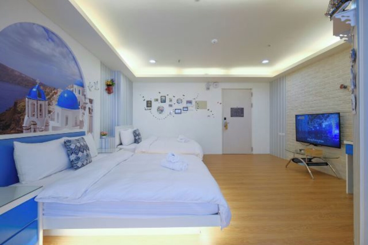 Een moderne hotelkamer met een groot bed, een flatscreen-tv en een muurschildering van een kustlandschap.