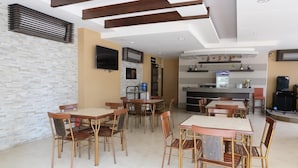 Un espacio interior amplio con varias mesas y sillas, un televisor de pantalla plana en la pared y una zona de bar con un refrigerador y estanterías.