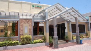 Entrada de un hotel con una galería techada, pilares de piedra y un letrero que dice "Le Grand".