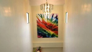Una escalera con peldaños de madera y barandales negros que lleva a un rellano con una araña y un cuadro abstracto y colorido.