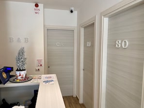 A hotel reception area with a desk, a potted plant, and a sign indicating the reset of the SOS and WC buttons. - BeB Caruso (Sorrento)